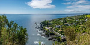 Vista panorâmica da Caloura, casas brancas junto à enseada, vegetação verde e mar azul na costa sul de São Miguel.