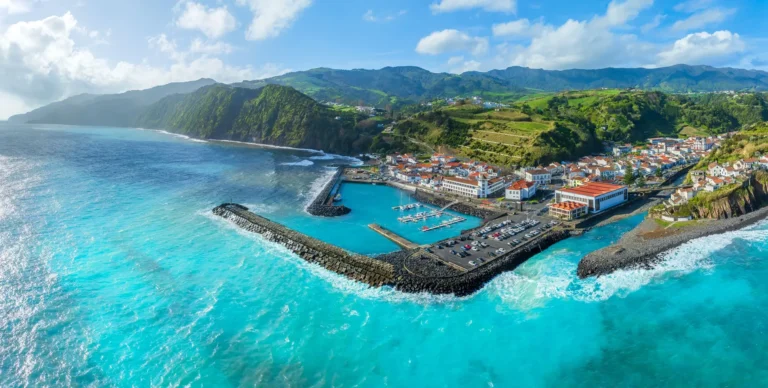 Vista aérea da vila e porto da Povoação, mar azul, casas tradicionais e montanhas verdes de São Miguel.