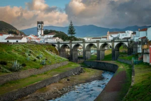 View of Ribeira Grande with stone bridge, river, historic town and mountain backdrop on São Miguel Island.